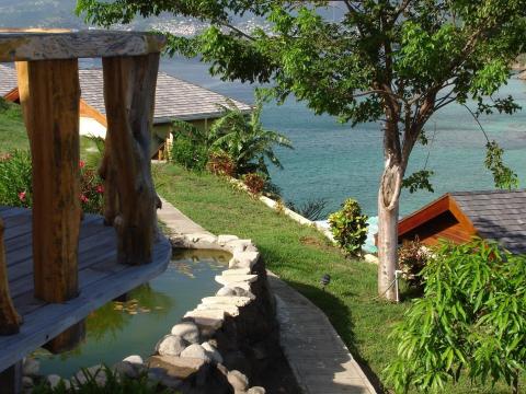 Tranquil pond and lush garden by serene lake with rustic shelter and manicured lawn.