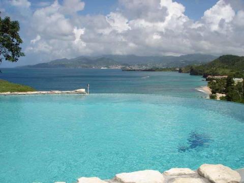 Infinity pool merging with ocean, tropical coastline in background, clear sunny day