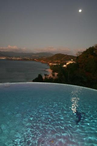 Twilight view of infinity pool overlooking serene coastal bay with moonlit sky.