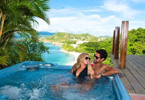Couple relaxing in jacuzzi overlooking tropical beach with serene bay view