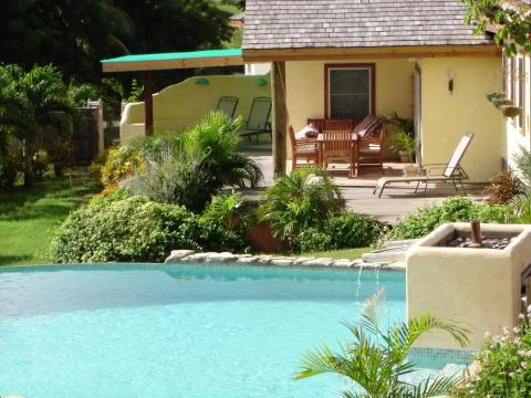 Elegant backyard with pool, yellow house, and tropical plants, ideal for relaxation.