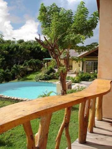 Serene wooden porch leading to yellow house with kidney-shaped pool and lush garden