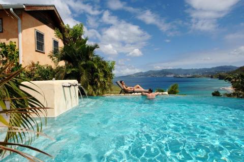 Two people relax by an infinity pool overlooking a coastal landscape.