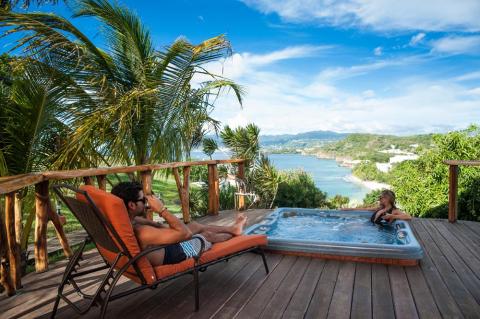 Woman in hot tub and man lounging on a deck overlooking a tropical bay