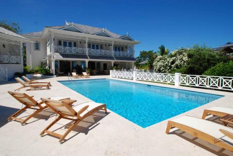 Luxurious poolside with sun loungers by an elegant white house and lush greenery on a sunny day