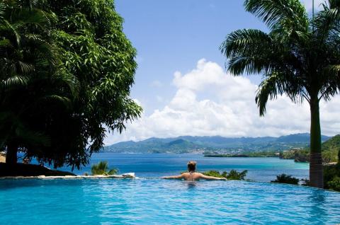 Person relaxing in infinity pool overlooking tropical bay and lush hills