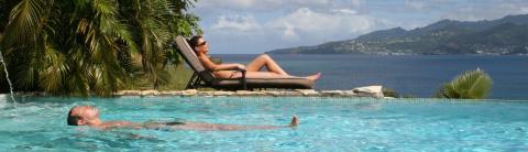 Woman sunbathing, man swimming in infinity pool overlooking ocean and mountains