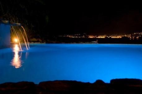 Illuminated pool with waterfall feature at night, cityscape in the background
