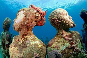 Underwater statues in coral reef serve as marine habitat and diver attraction.
