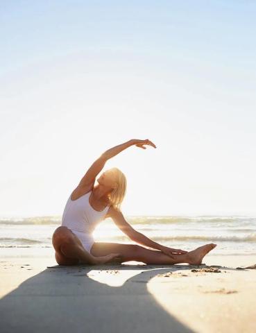 Person doing yoga on beach at sunset, silhouetted by warm light