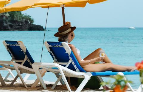 Person relaxing on beach chair by sea under sunshade with drink