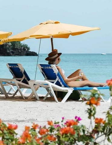 Woman relaxing on beach chair under umbrella with sea view, holding a drink