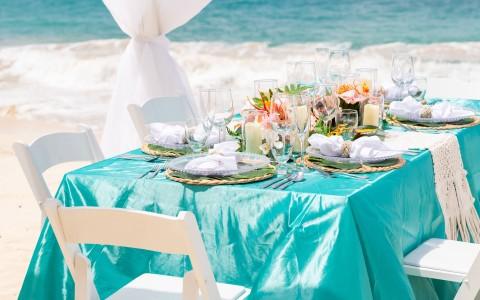 Beachfront dining setup with turquoise tablecloth and tropical centerpiece