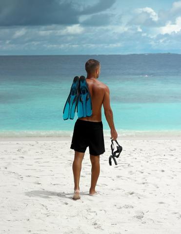 Man with flippers and snorkel on beach ready to swim in the sea