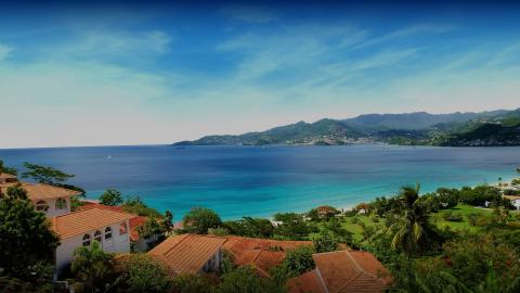 Tropical coast view with terracotta roofs, clear blue sea, and lush greenery