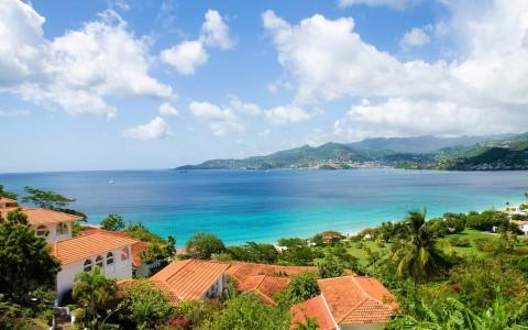 Coastal scene with red-roofed houses, lush greenery, and turquoise sea