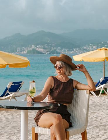 Woman with cocktail at beach table enjoying sunny vacation scene