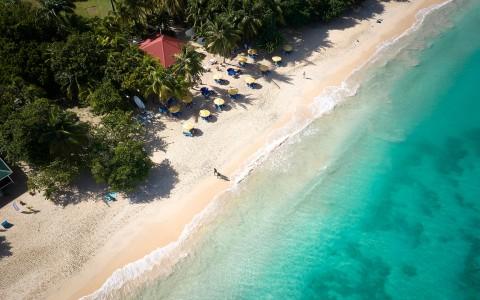 Aerial view of tropical beach with colorful umbrellas, clear waters, and lush greenery.
