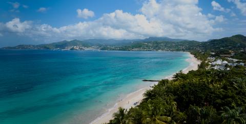 Coastal landscape with turquoise sea, sandy beach, umbrellas, palm trees, and mountain backdrop