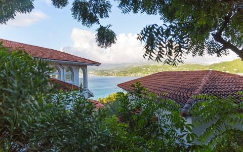 Scenic coastal view from elevated balcony with red-tiled roofs and lush foliage
