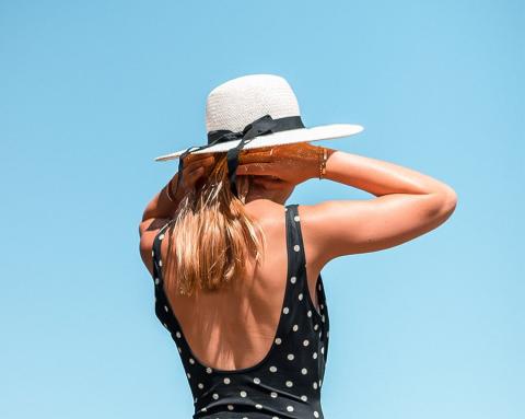 Woman in polka dot top and white hat holding hat under blue sky