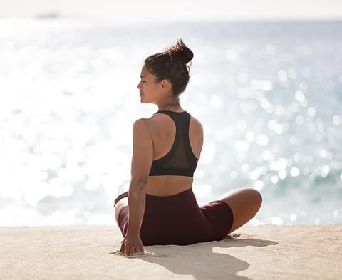 Woman meditating by sea in yoga attire, sunny day, serene ocean backdrop.