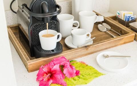 Coffee machine dispensing coffee, white mugs, and sugar on a wooden tray with hibiscus decor.
