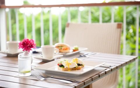 Outdoor breakfast with eggs benedict, coffee, and a scenic view on a patio.