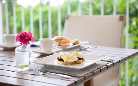 Outdoor breakfast setting with Eggs Benedict and scenic greenery backdrop.
