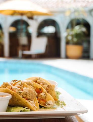 Plate of chicken tacos by a pool, enhancing a tropical resort dining experience