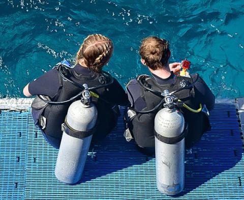 Two scuba divers with gear on blue dock ready for underwater adventure
