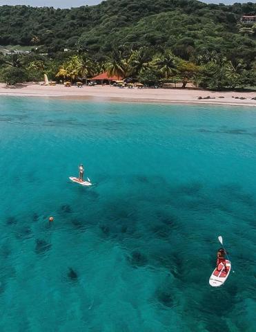 Aerial view of two people paddleboarding in tropical blue waters near a sandy beach.