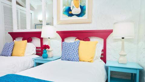Bright magenta headboard twin beds with tropical decor in colorful bedroom.