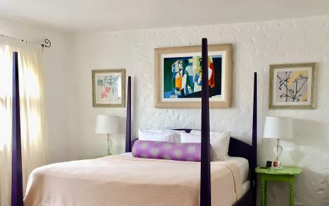 Elegant bedroom with large poster bed, nightstands, lamps, and vibrant artwork.