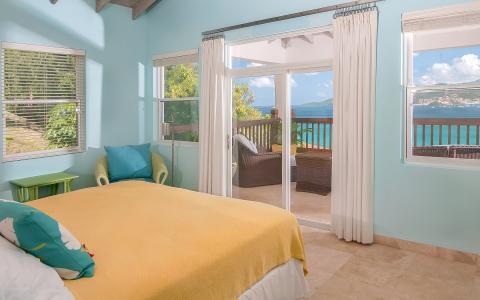 Bright bedroom with sea view, yellow bedspread, and balcony seating area