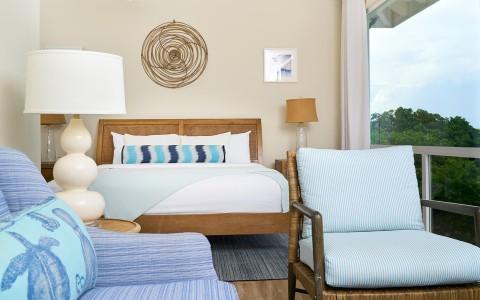 Bright, airy bedroom with double bed, striped pillows, and green landscape view.