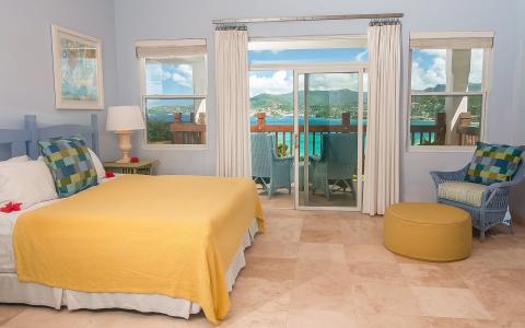 Cozy bedroom with yellow blanket, scenic view balcony, coastal town backdrop.
