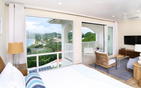 Scenic resort room with balcony view, bed and wicker seating area.