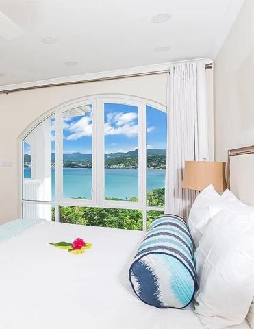 Coastal bedroom with scenic view, white linens, striped pillow, and sea landscape.