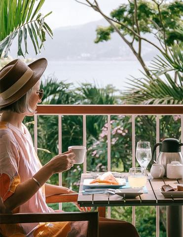 Person having breakfast on balcony with scenic lake view, tropical setting
