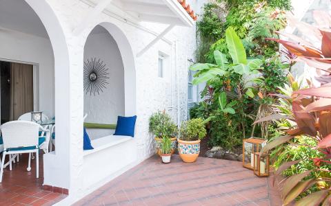 Charming outdoor patio with white furniture, terracotta tiles, and lush greenery.