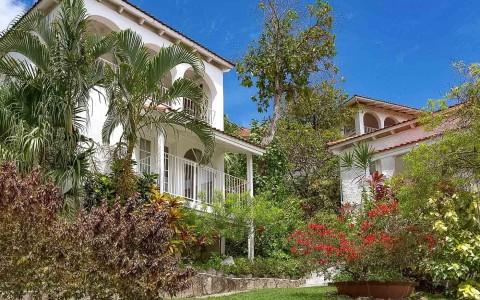 Tropical residential scene with white houses, red tiles, lush gardens, and hibiscus flowers.