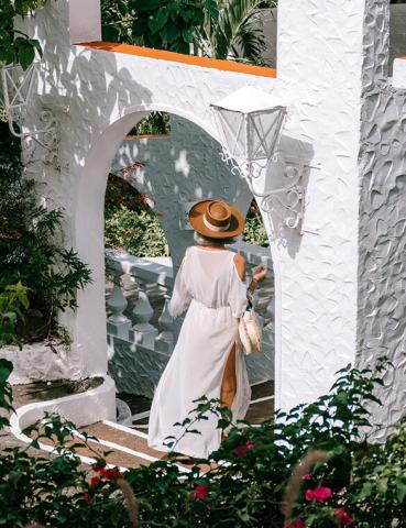 Woman in white dress walking through ornate garden archway with lush plants