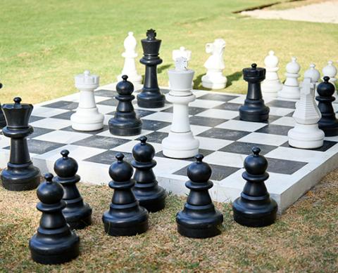 Outdoor large chess set in progress on grass in park, black and white pieces.