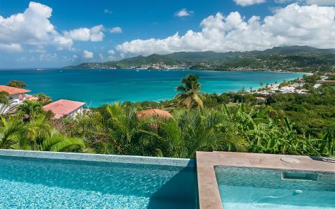 Luxury tropical resort with infinity pool overlooking a vibrant coastal town and turquoise sea