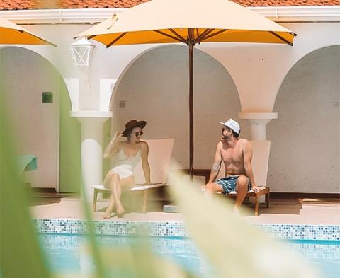 Relaxed poolside scene with two people under yellow umbrellas, tranquil setting.