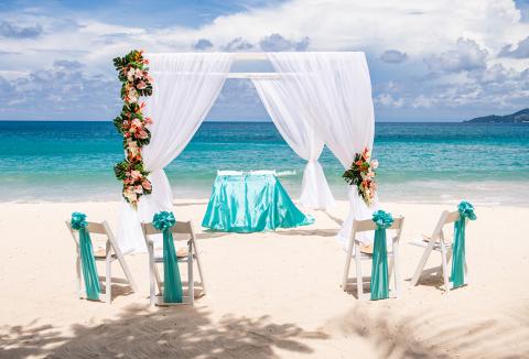 Scenic beach wedding setup with white arch and teal accents overlooking the ocean.