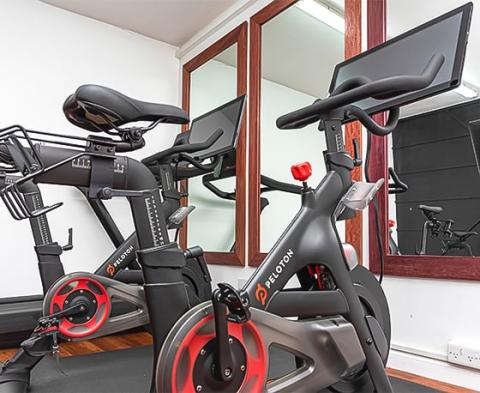 Two Peloton bikes in a private gym with wooden floors and a mirror.