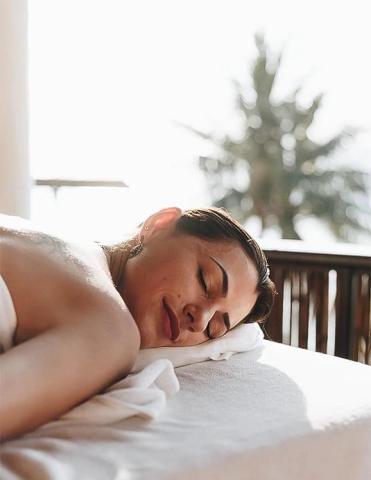 Person resting on a towel outdoors, peaceful with natural light and blurred greenery background.