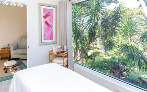 Spa room with massage table, garden view, cozy decor, and pink artwork for relaxation.